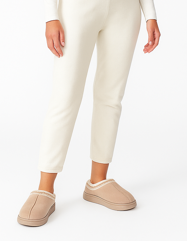 Person wearing beige slippers and white pants on a white background