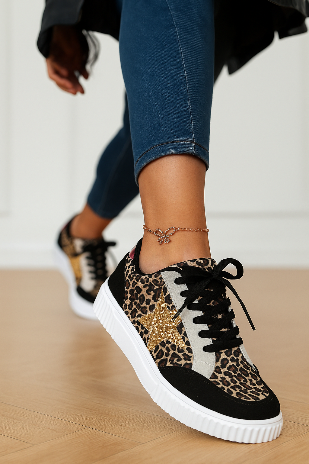 Leopard print sneakers worn with blue jeans on a light wooden floor.