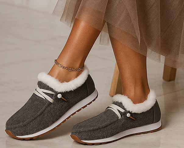 Gray slippers with white fur trim worn by a person on a neutral background