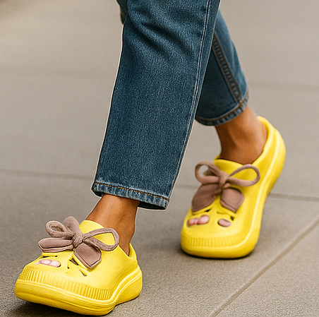 Yellow shoes with brown bows worn with blue jeans on a neutral background