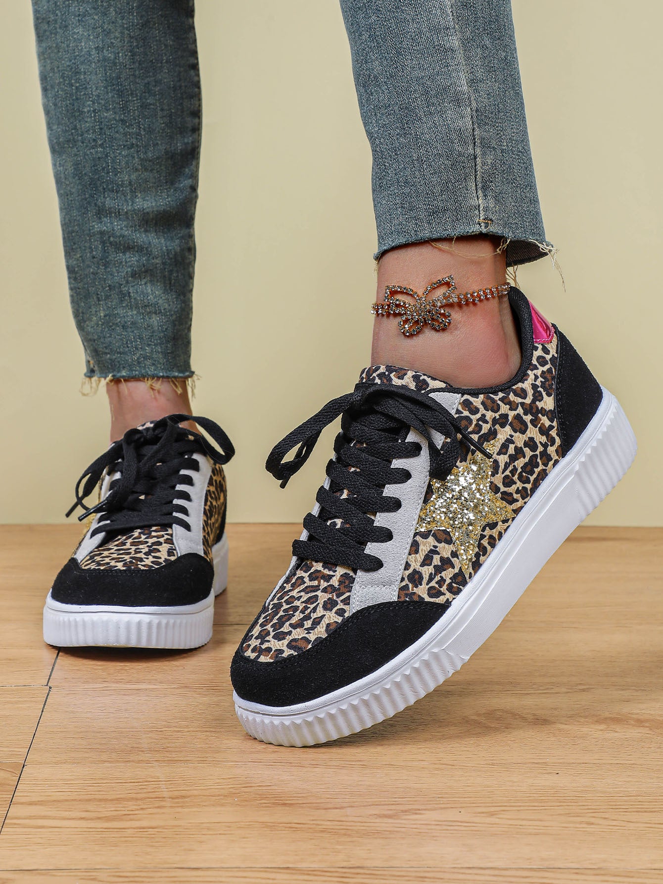 Leopard print sneakers with black and white sole worn by a person on a wooden floor.