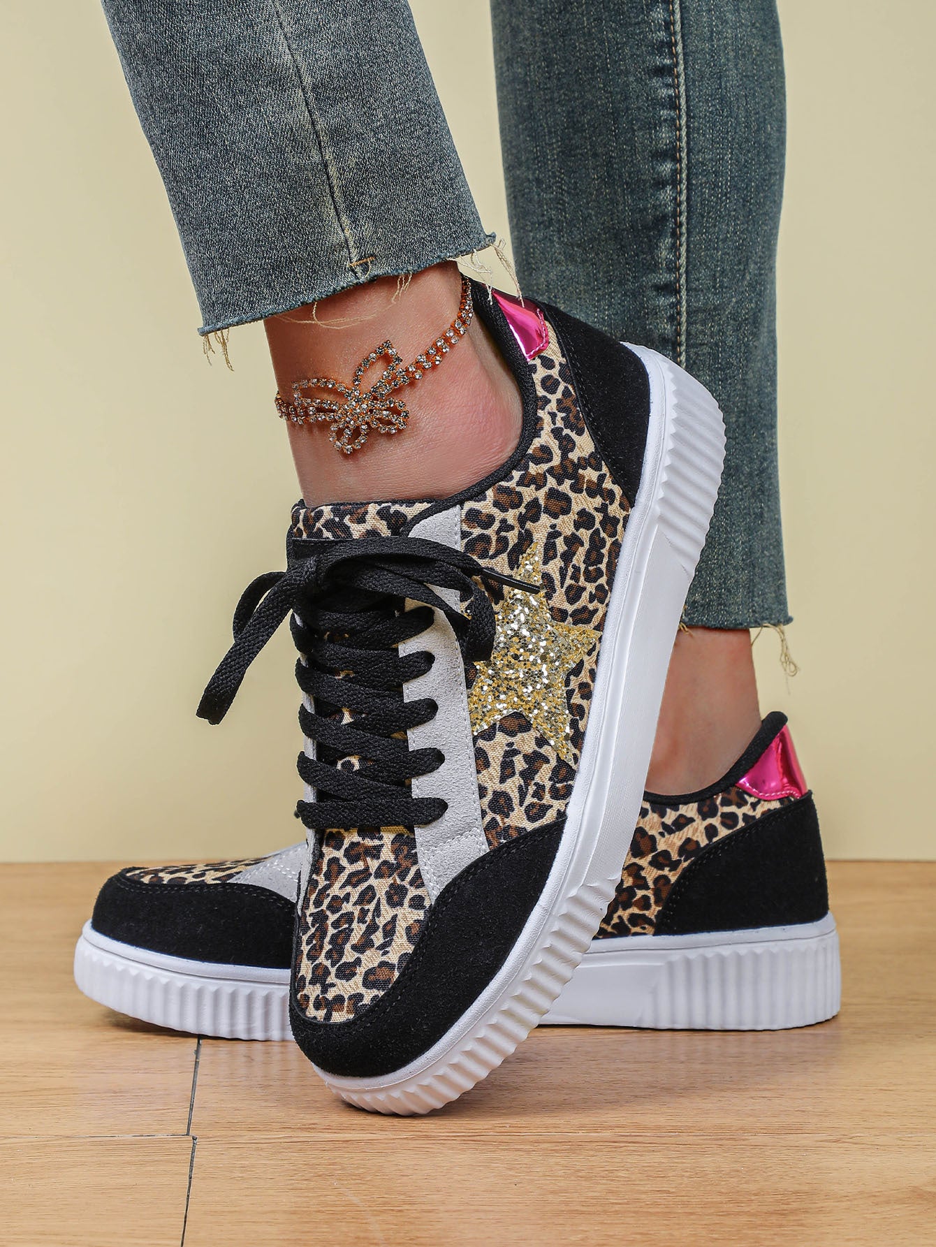 Leopard print sneakers with black and white accents worn by a person on a wooden floor.