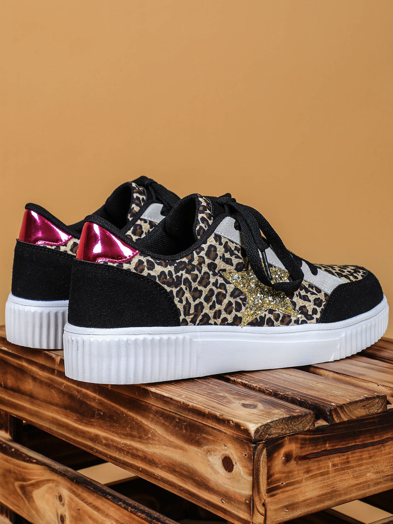 Black sneakers with leopard print and red accents on a wooden pallet against a brown background
