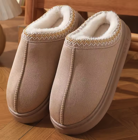 Pair of beige slippers with white fur lining on a wooden floor.