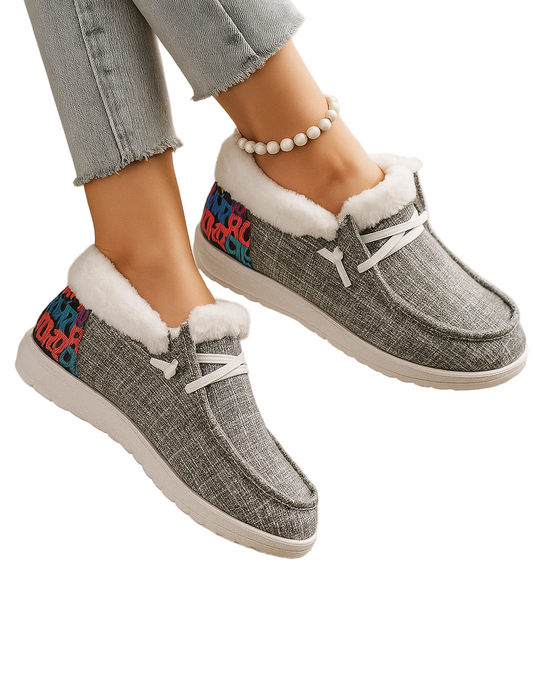 Gray slip-on shoes with colorful accents worn by a person on a light wooden floor.