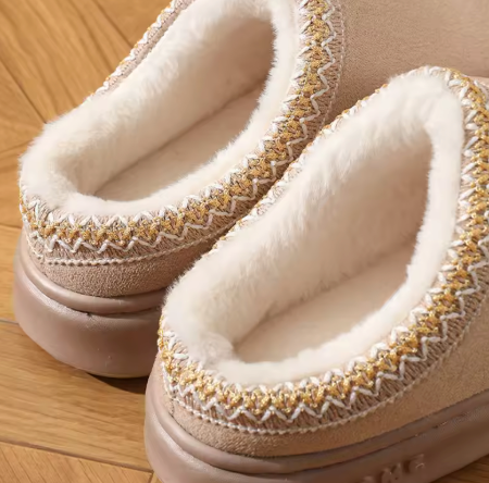 Pair of beige slippers with white fur lining on a wooden floor